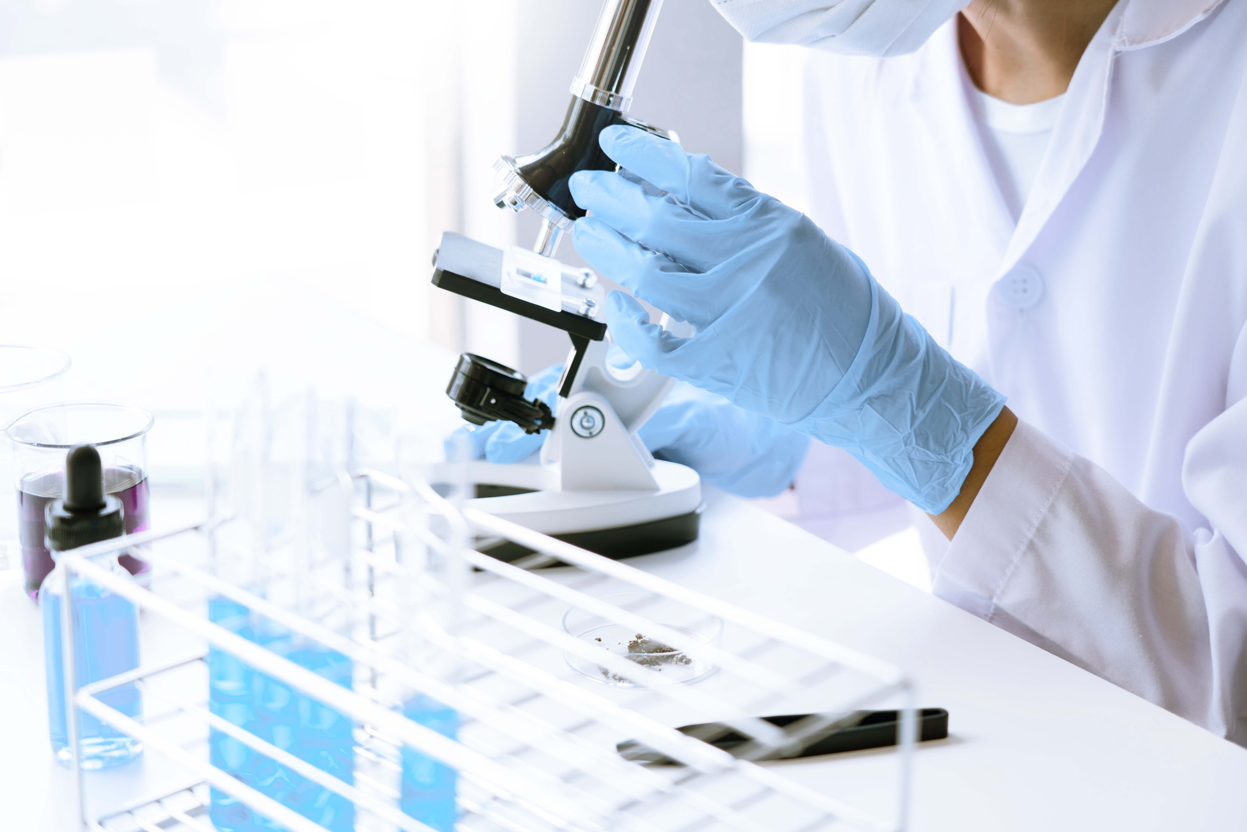 a hand wearing blue gloves holding a microscope