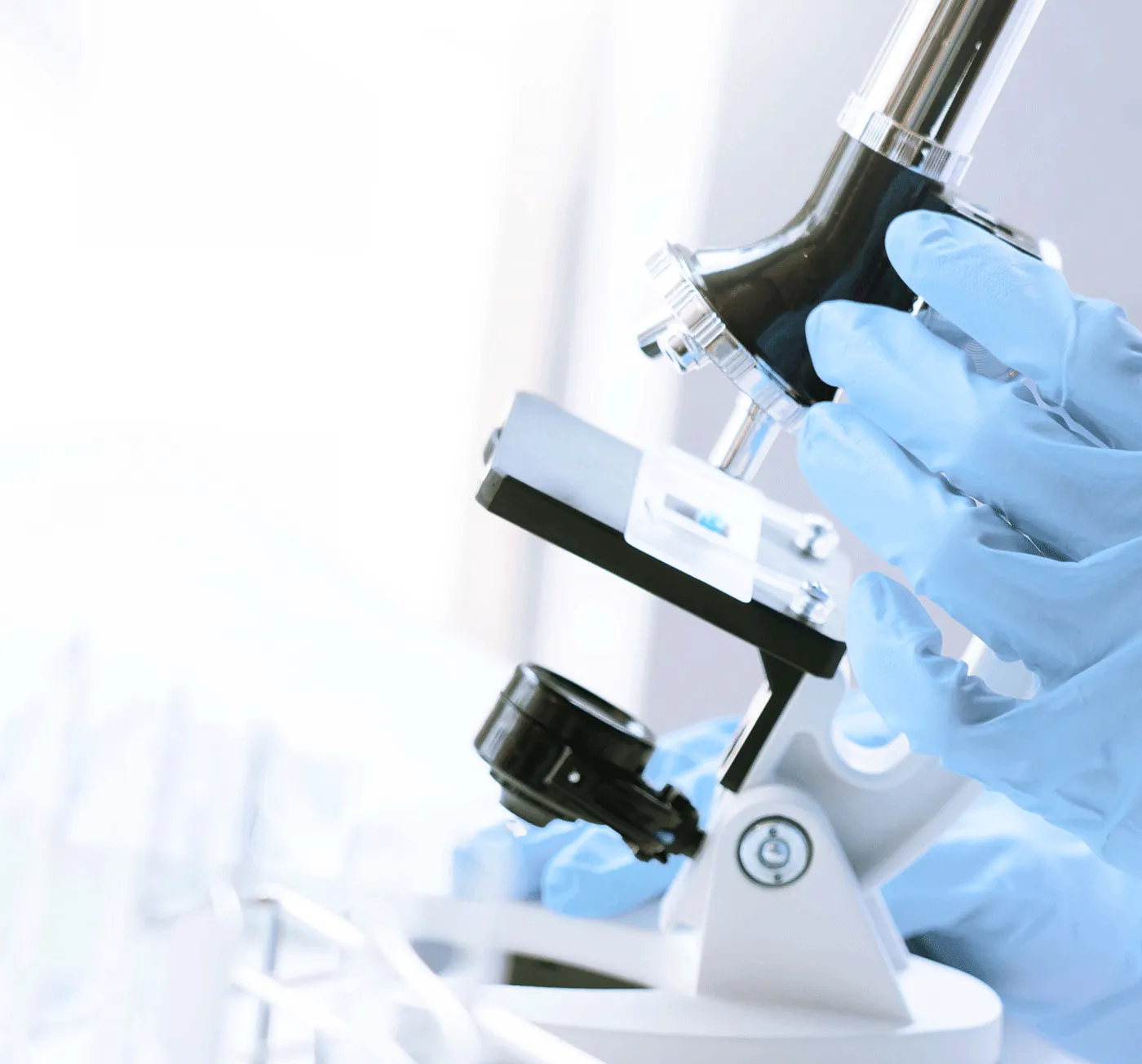 a hand wearing blue gloves holding a microscope